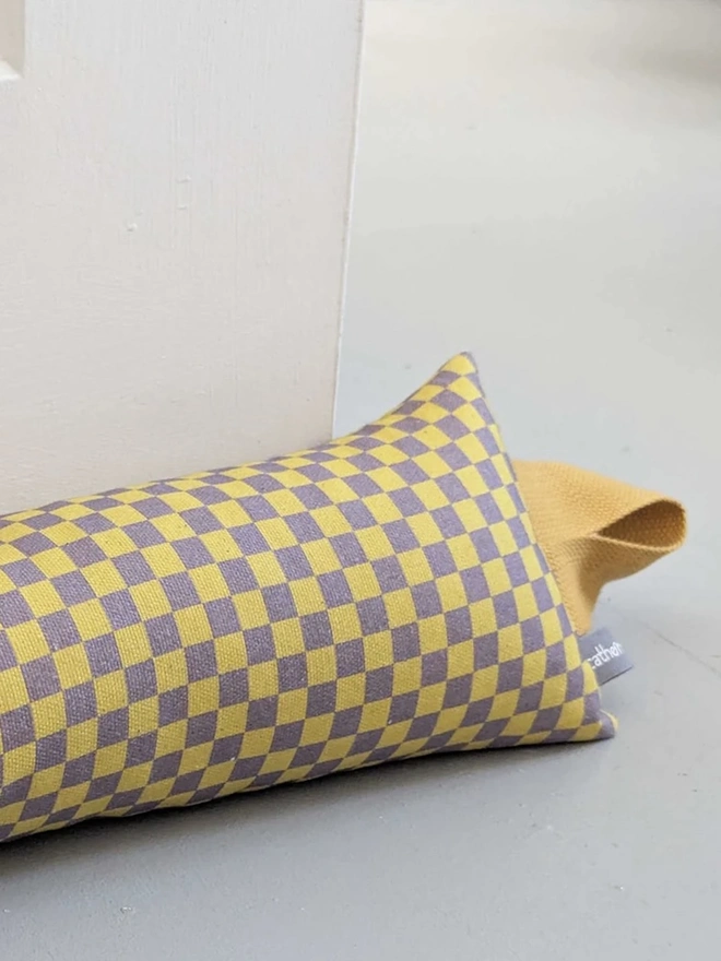 Draught Excluder, a colourful patterned draught excluder sitting on the floor by a white door. 