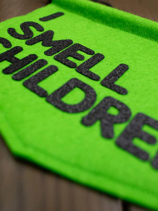 Close up of a green, felt halloween banner that has "I SMEEL CHILDREN" written on it in black glitter felt.