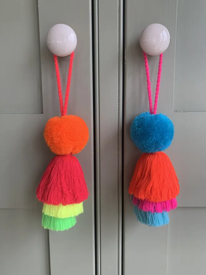 pom pom and tassel swag hanging decoration. hanging decorations in shades of blue, orange and neons hung on pink handles.