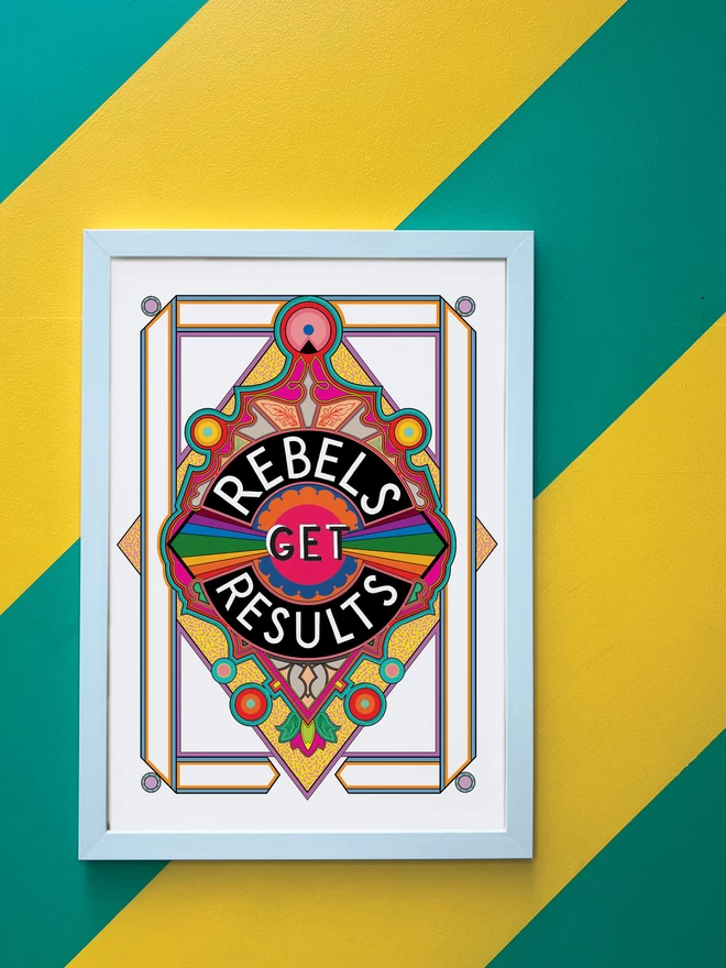 Rebels Get Results is written in white on a black background at the centre of this vibrant, abstract portrait illustration, with a white background and rainbows emitting from the centre, and multi-coloured detailing. The picture is hanging in a white portrait frame against a wall painted with thick diagonal green and yellow stripes.