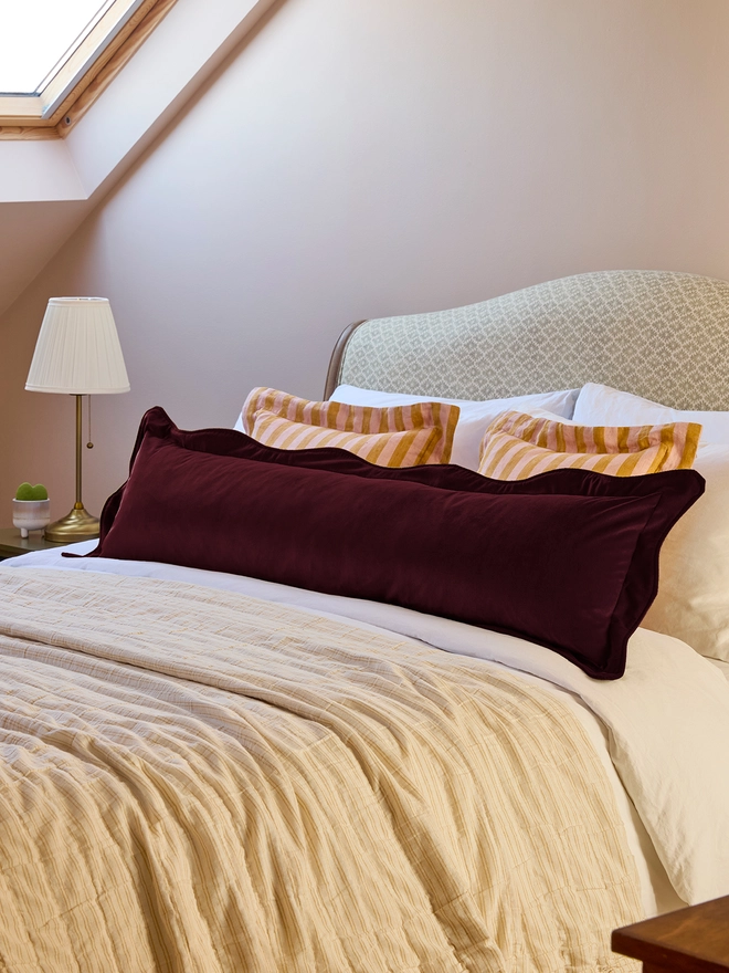 Handmade scalloped burgundy velvet bolster cushion 130cm with feather pad paired with stripe linen cushions on bed, Kika Bespoke