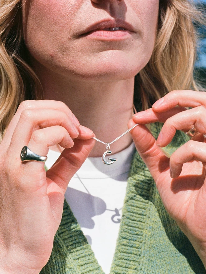 a woman holds a thin silver chain with a handmade silver 'G' pendant