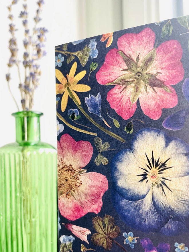 Close-Up of Dark Blue Pressed Flower Greetings Card with Green Glass Bottle on Windowsill