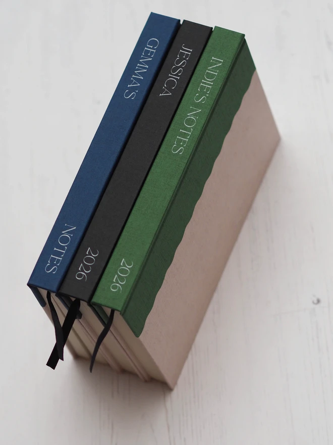 three hardcover journals stacked on their side showing personalised text down the spine of the book in white ink