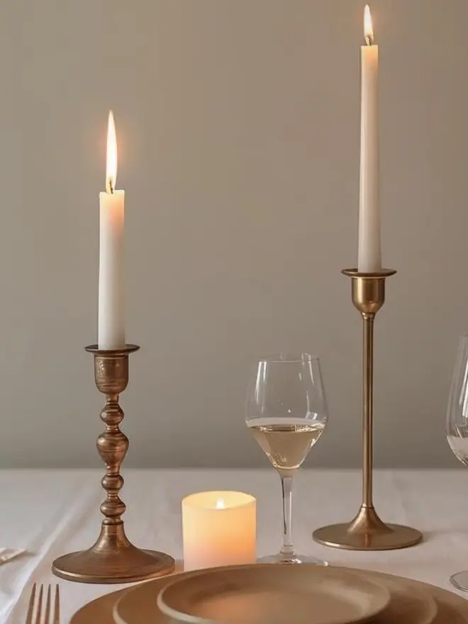 Lifestyle image of two white dinner candles on a table cloth with brass dining set