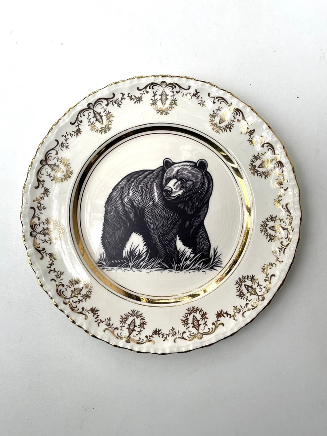 a vintage plate with an ornate border, in the centre of the plate is a vintage style black and white illustration of a big bear