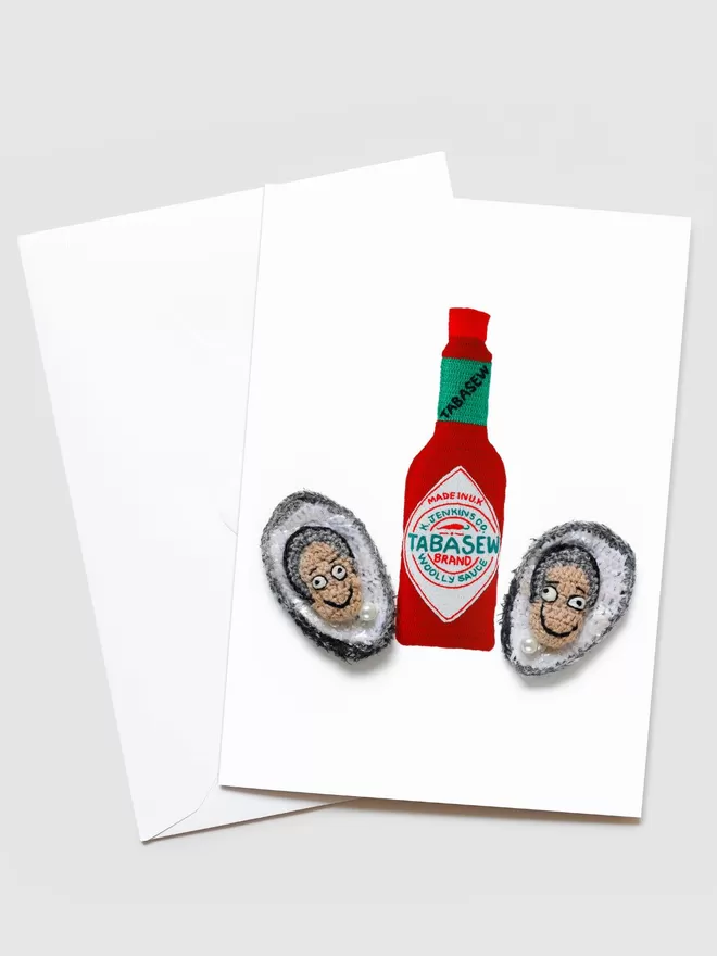 Kate Jenkins Oysters Card seen with a blank envelope. On the front of the card are two half oysters with faces inside and a Tabasco bottle in the middle.