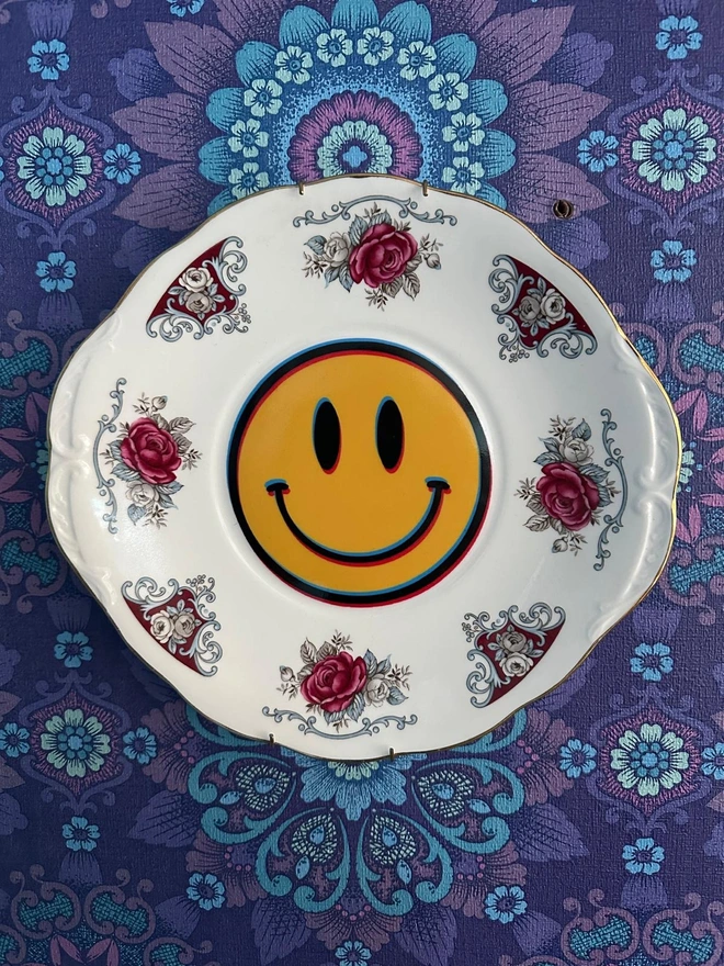 A round plate with a border of roses and a yellow smiley face in the center