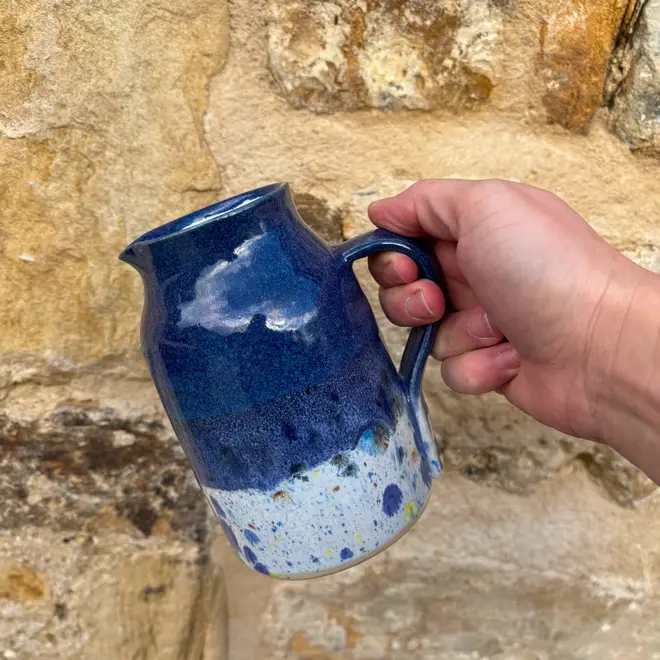 Shoreline Medium Jug, a colourful jug being poured against a brick wall backdrop. 