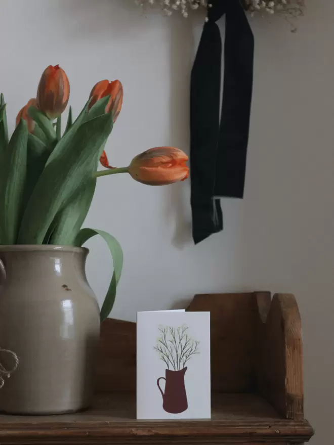 card next to a vase of tulips sat on a wooden shelf