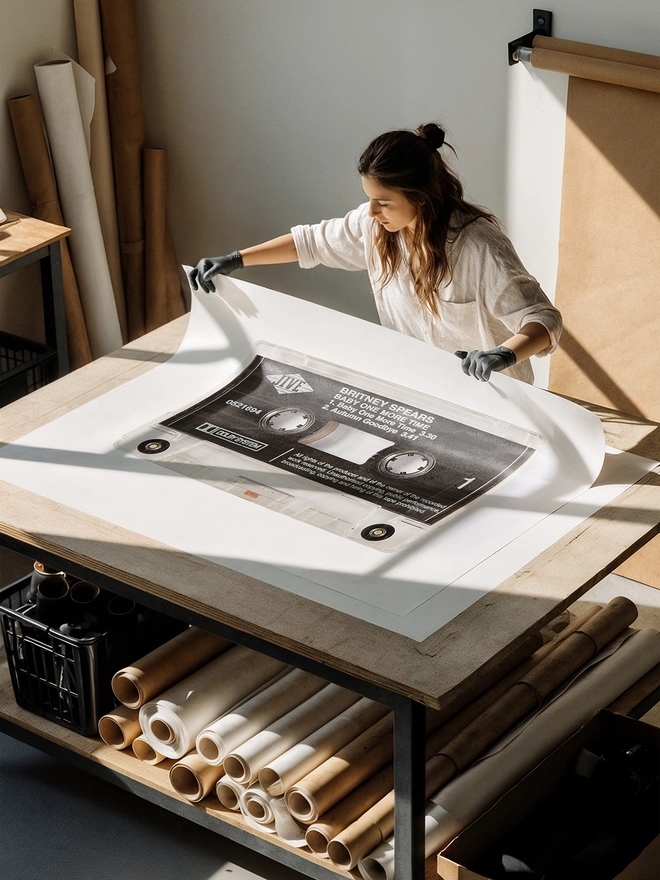baby one more time britney spears cassette print. artist unrolling print on studio table.