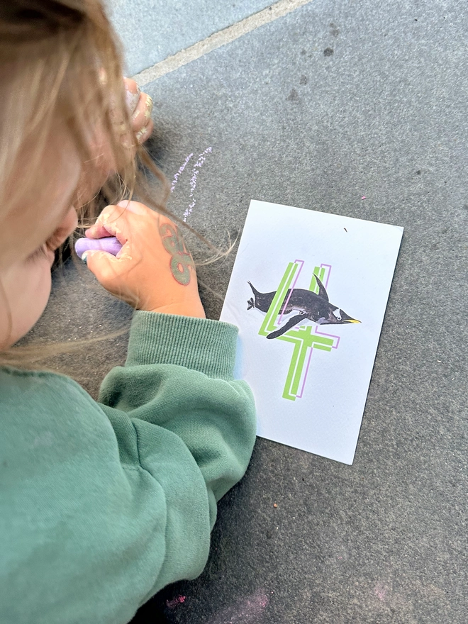 a white card with a big green number 4 and a penguin illustration with a child playing with chalk on the floor