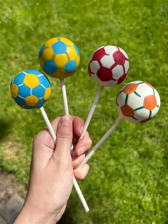 football cake pops. four cake pops shaped like football with various colours of icing. 