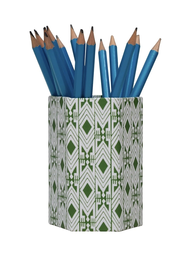 Tijan Hexagonal Brush Pot, a colourful patterned pencil pot sitting on a white surface against a plain backdrop. It is filled by some pencils. 