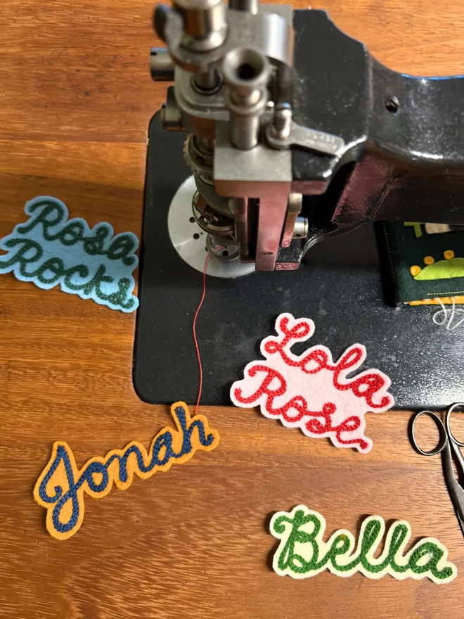 Four chain stitched embroidered patches on a wooden desk with an antique chain stitch machine