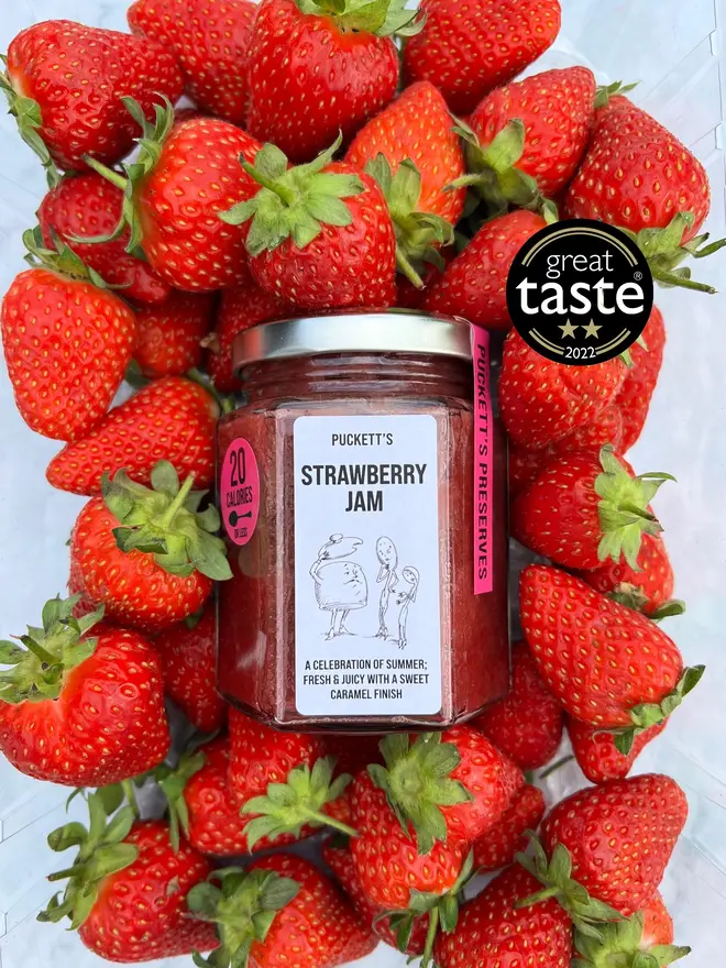 british strawberry jam. a jar of strawberry jam photographed among fresh strawberries.