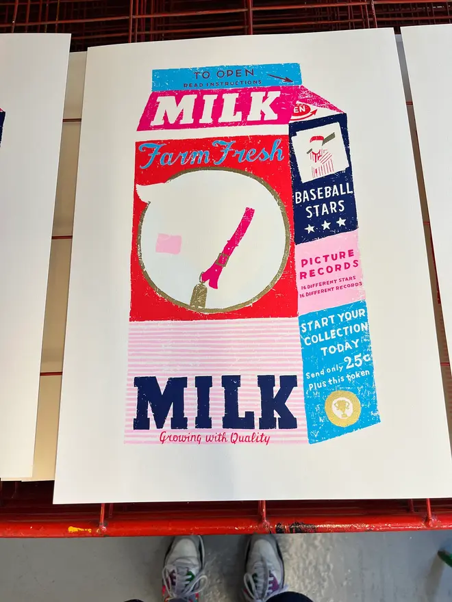 Milk Carton Cow Screenprint Daisy's Finest, a colourful milk carton design on a white screenprint. It sits on a studio rack. 