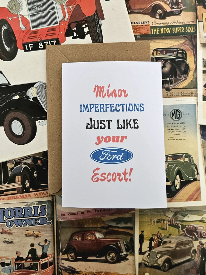 A birthday card that says minor imperfections just like your Ford Escort written in vintage style font on a white card. The colours of the words are green, blue, red and black