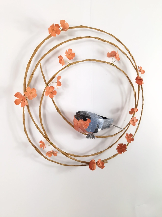 woodland wall hanging, depicting a bullfinch bird sculpture, on a wreath of peach blossom flowers