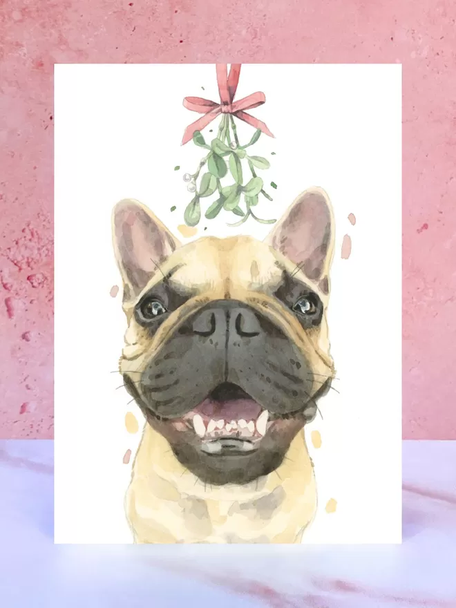 A Christmas card featuring a hand painted design of a 'Frenchie' French Bulldog, stood upright on a marble surface.