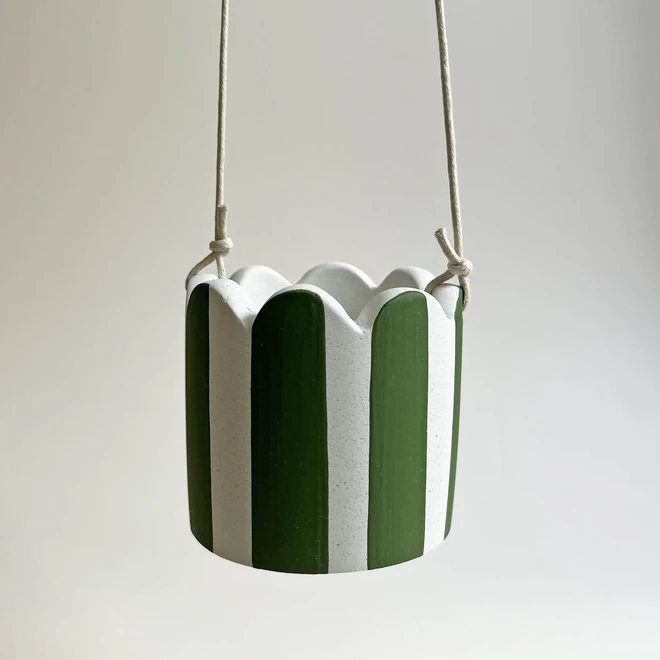 Green and white scalloped hanging pot. Made from Jesmonite. Hanging against a plain background.