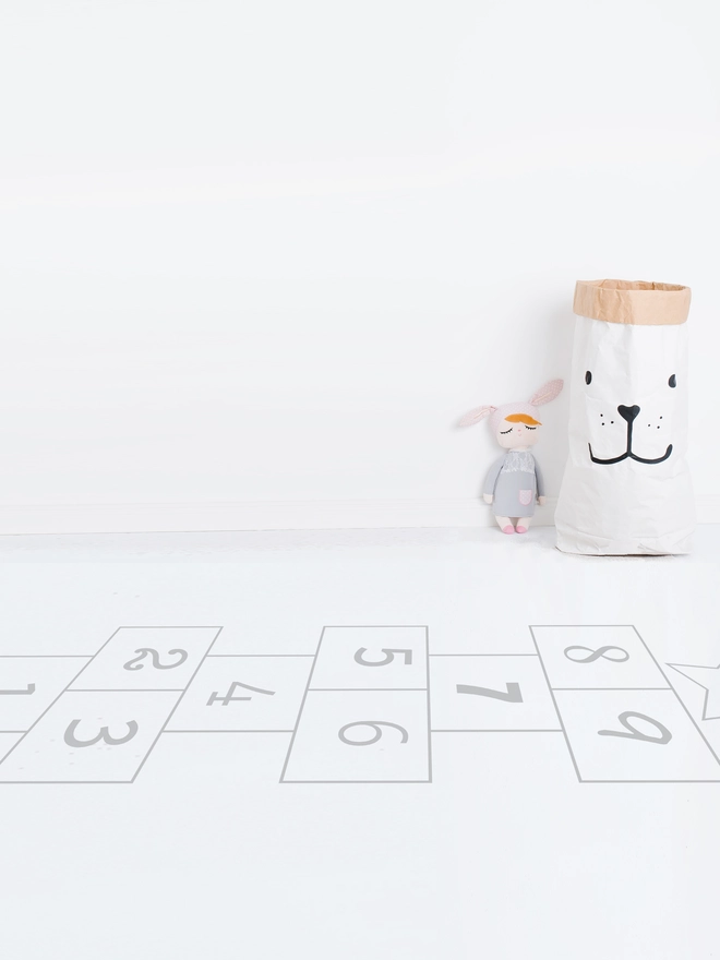 Hopscotch  numbers in black on a white floor with a teddy leaning against a white wall
