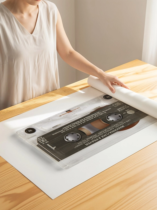 like a prayer madonna cassette tape print. print being unrolled on wooden table.