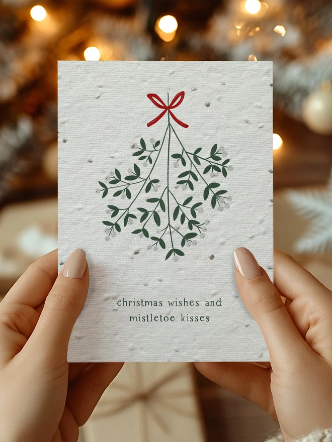 A pair of hands holding a Christmas card with mistletoe in the centre with 'Christmas Wishes and Mistletoe Kisses' written underneath.