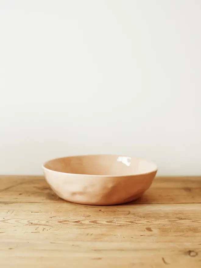'sunrise' handcrafted stoneware bowls. a medium pink bowl on a wooden bench.