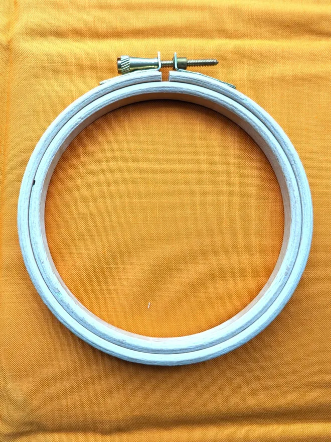 A wooden embroidery hoop lying on a piece of orange coloured fabric