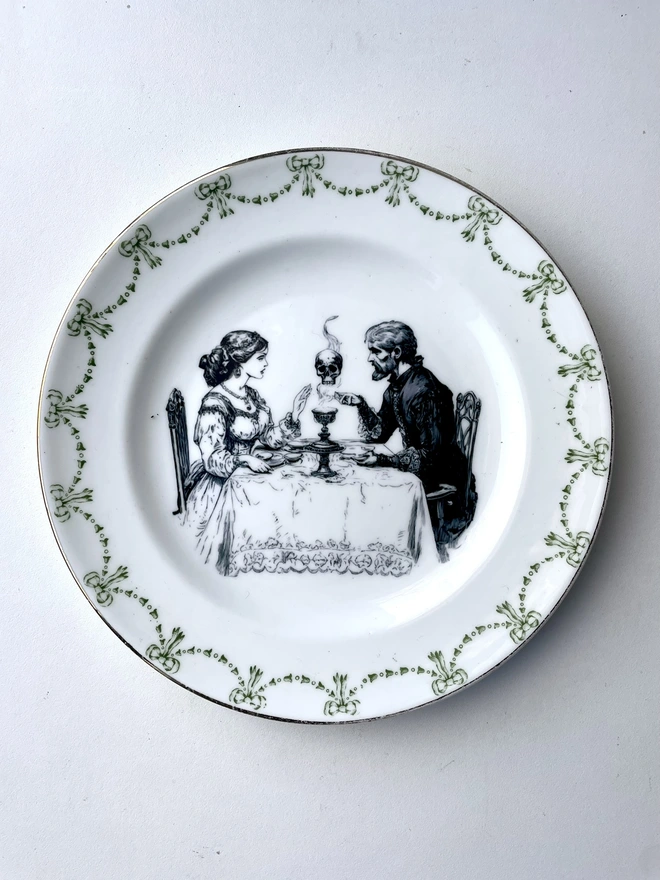 a vintage plate with an ornate edge, in the centre is a vintage illustration of a victorian man and lady drinking tea and summoning up spirits