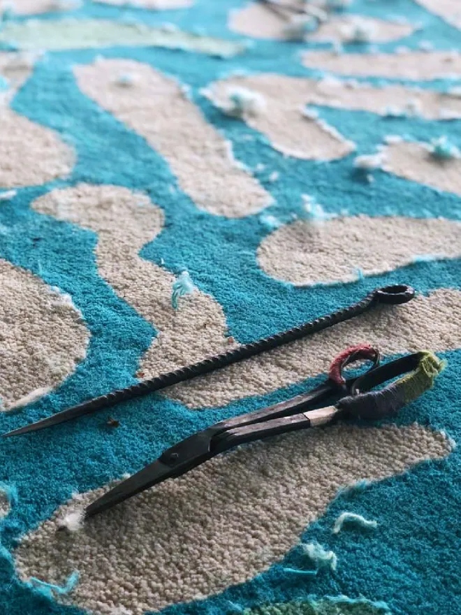 Scissors and tools used to hand carve rugs, sitting on a blue plush wool rug
