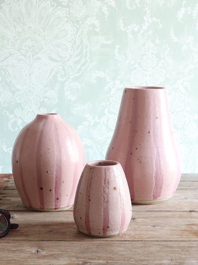 A collection of three Handmade Ceramic Stoneware Vases in Pink Stripe in three sizes: small, medium and large sat on a wooden surface