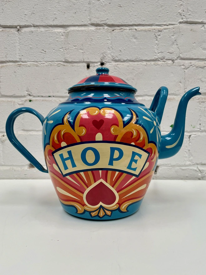 Large blue vintage enamel teapot, hand-painted with a traditional fairground inspired design in pink, yellow and orange. 'Hope' is painted in a banner across the centre.