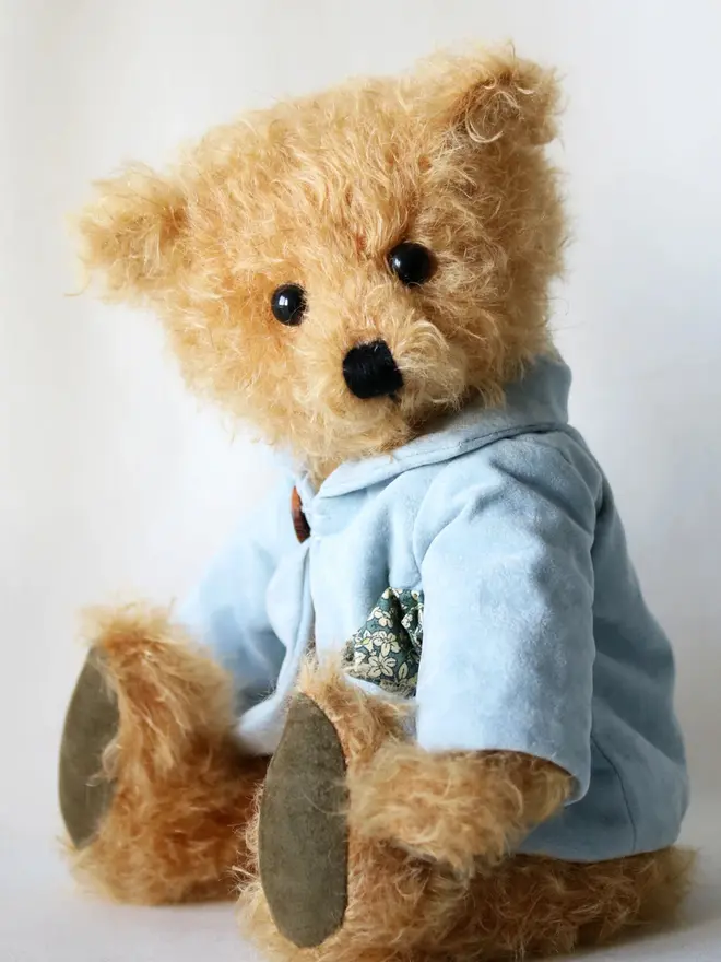 Handmade teddy bear with soft textured fur, wearing a blue jacket, posed against a plain background.