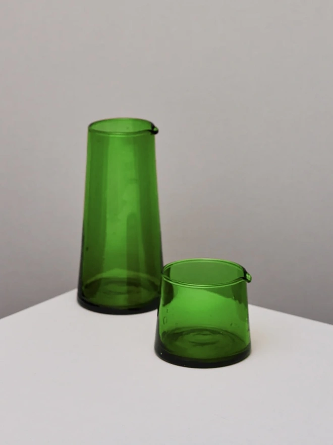 Glass Jugs (Set Of 2), a pair of a large and small green glass jar sitting on a plain counter top against a grey backdrop. 