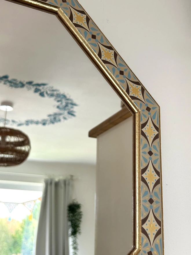 Medium sized octagonal wall mirror with a hand painted decorated frame with gold stars and blue star burst repeating pattern around the frame