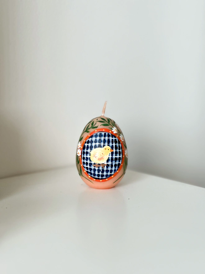 Hand Painted Easter Egg Candle Chick, an Easter egg candle sitting on a plain surface. It's Easter and floral design wraps around the egg. 