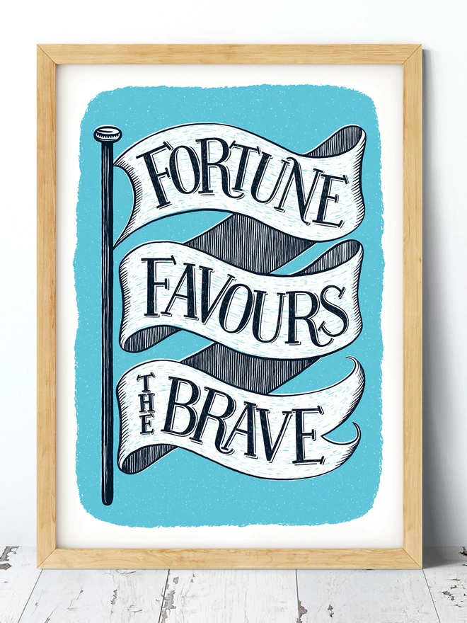 fortune favours the brave print in blue and white in a wood frame on a white washed floor