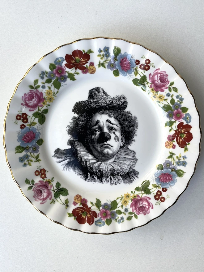 a vintage plate with an ornate border, the middle has a black and white vintage illustration of a sad clown in the middle