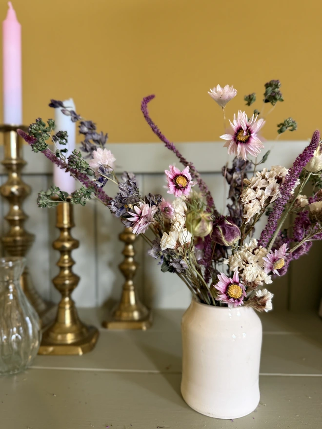 a selection of dried flowers in a ceramic vase on a shelf with candles in brass candlesticks