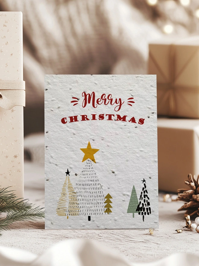 Christmas card with Christmas trees and 'Merry Christmas' on surrounded by presents in a Christmas scene