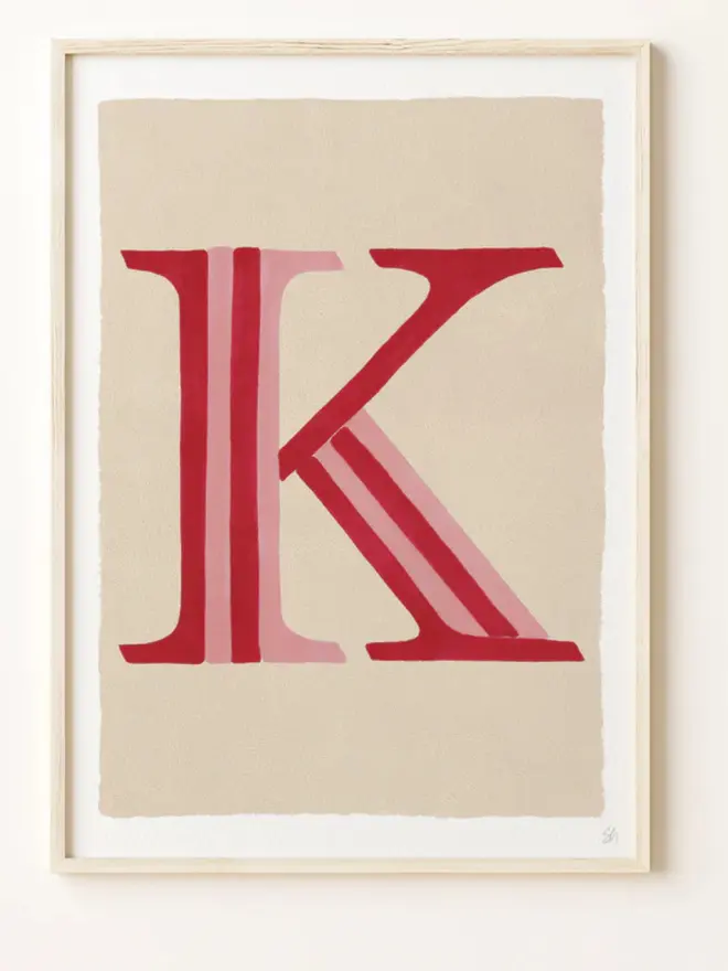 Framed wall art print featuring a large decorative letter “K” in humbug stripes
centered on a white background. 