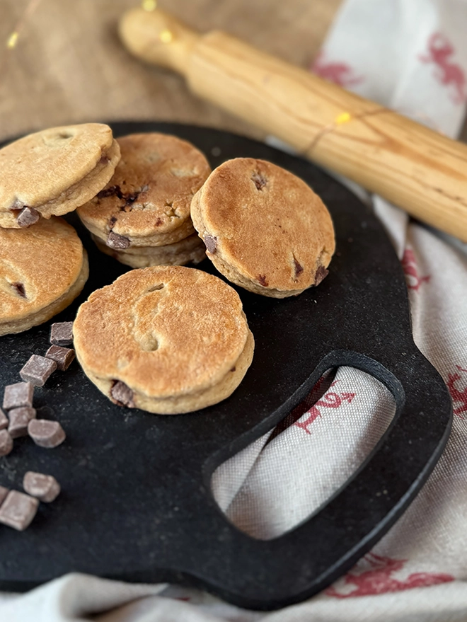 Chocolate Chip Welsh Cakes on a bake stone griddle with chocolate chips and a wooden rolling pin