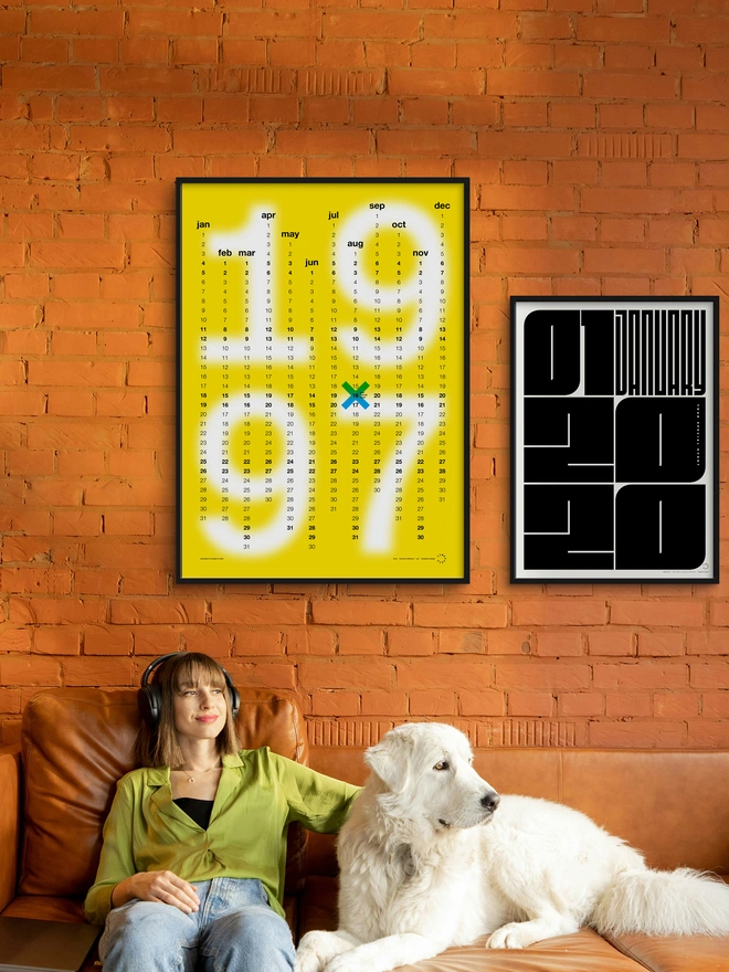 Yellow Minx Personalised Date Poster on orange wall, above a person and a dog sitting on an orange sofa