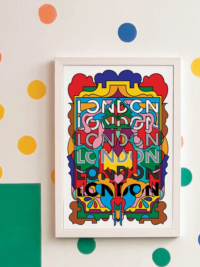 A vibrant, portrait print containing all the colours of the London Underground lines, with the word London repeated six times from top to bottom. The picture is hanging in a white frame on a white wall, with yellow, orange, green and blue spots and a green rectangle painted in the bottom left hand corner.