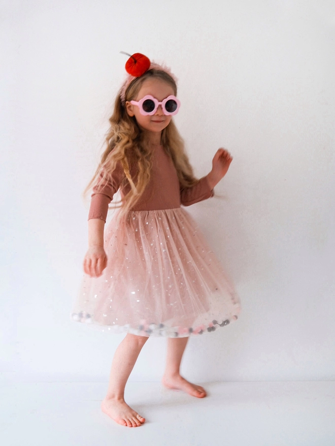 Young girl posing wearing sunglasses and a pom pom tutu dress