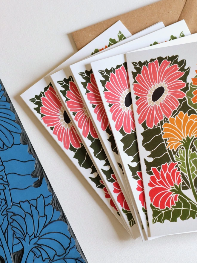 Hand-carved lino block displayed with finished African Gerbera daisy flower notecard from set of 8. Traditional relief printmaking block showing carved botanical design. Authentic linocut process, Norfolk countryside studio
