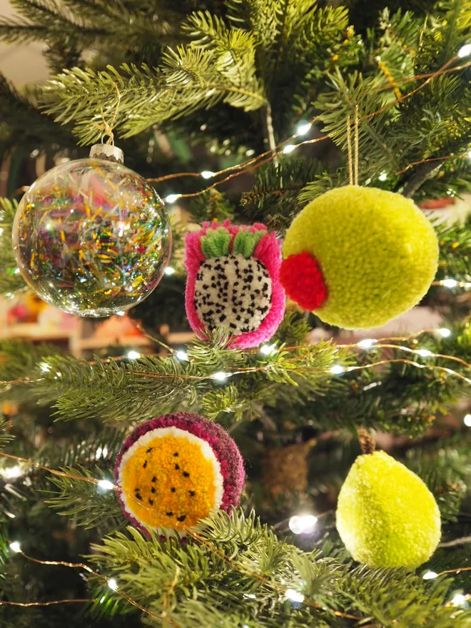 Handmade Passionfruit Pom Pom Bauble hanging on a tree with other pom pom baubles