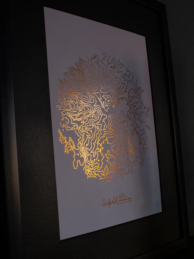 Framed metallic copper contour map of Sheffield, with the light catching the print